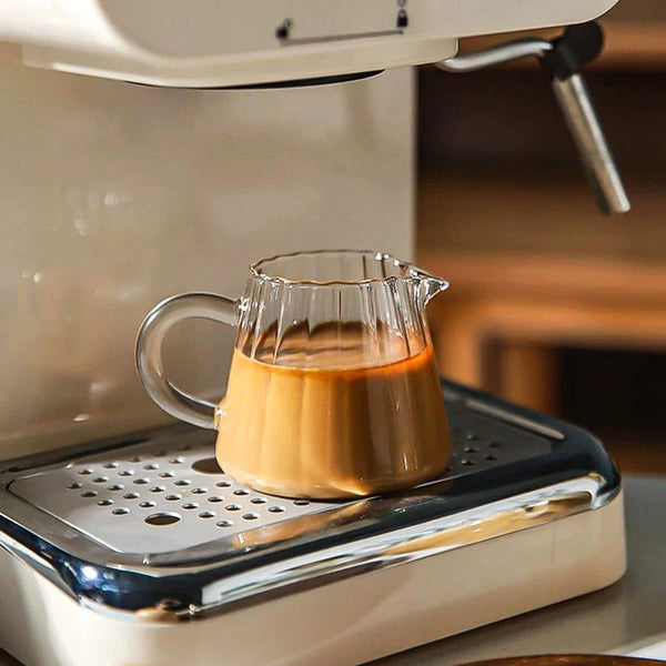 A striped borosilicate glass milk pitcher is sitting on a white appliance, ready for use.