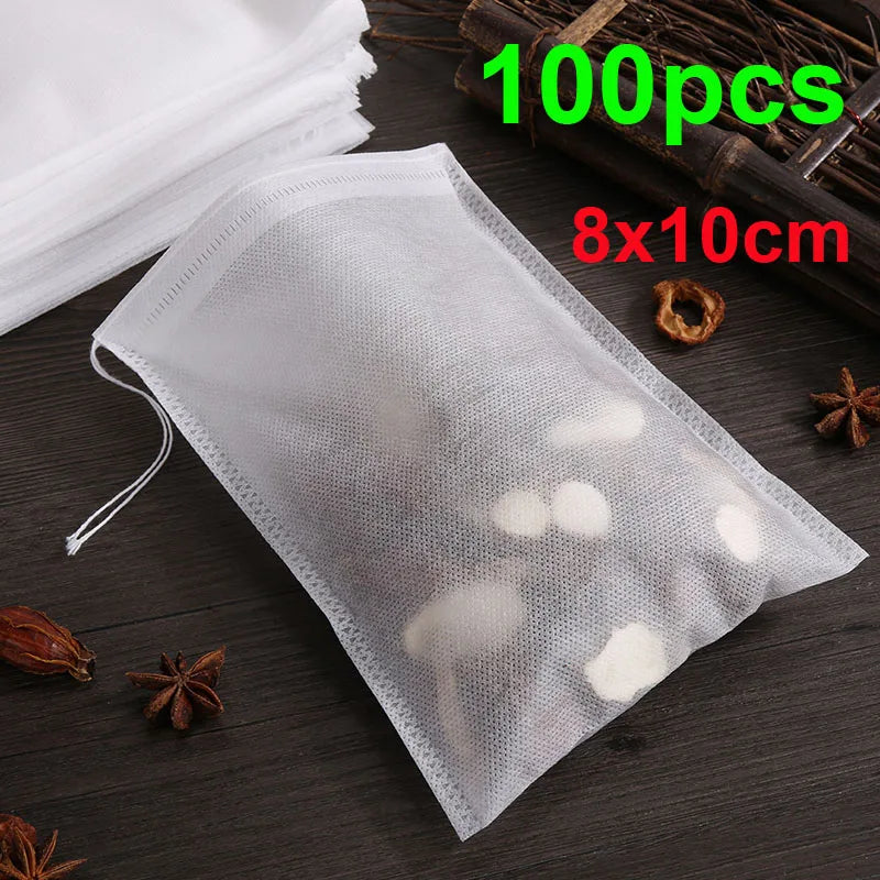 A clear plastic disposable tea filter bag with a drawstring is shown on a dark surface, next to dried spices and a wooden too