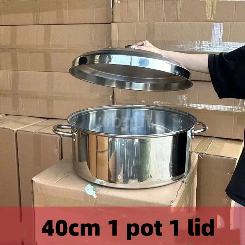 A hand is lifting the lid of a large stainless steel pot with a matching lid, resting on a cardboard box.