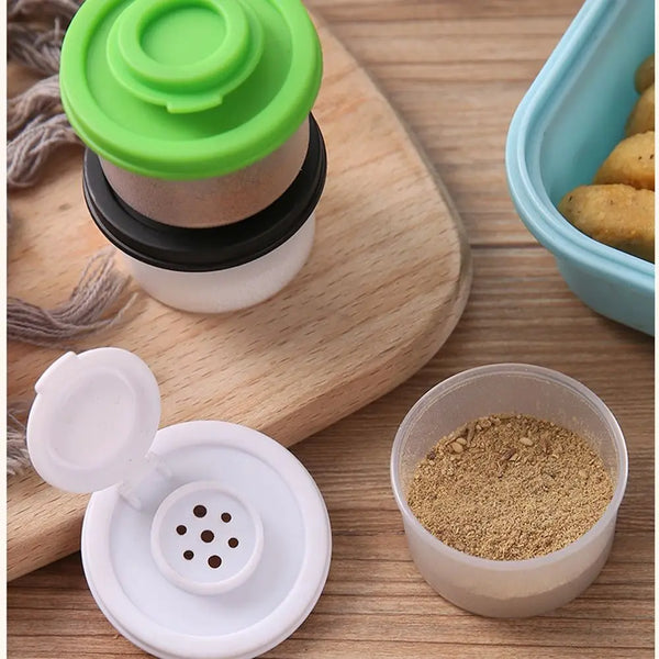 Ein Set aus vier Mini-Gewürzstreuern in verschiedenen Farben und Materialien auf einer Holzoberfläche.