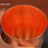 A close-up view of a handcrafted vintage copper coffee mug with a bright orange interior.