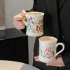 A person holds a white ceramic coffee mug with a floral pattern against a dark background.