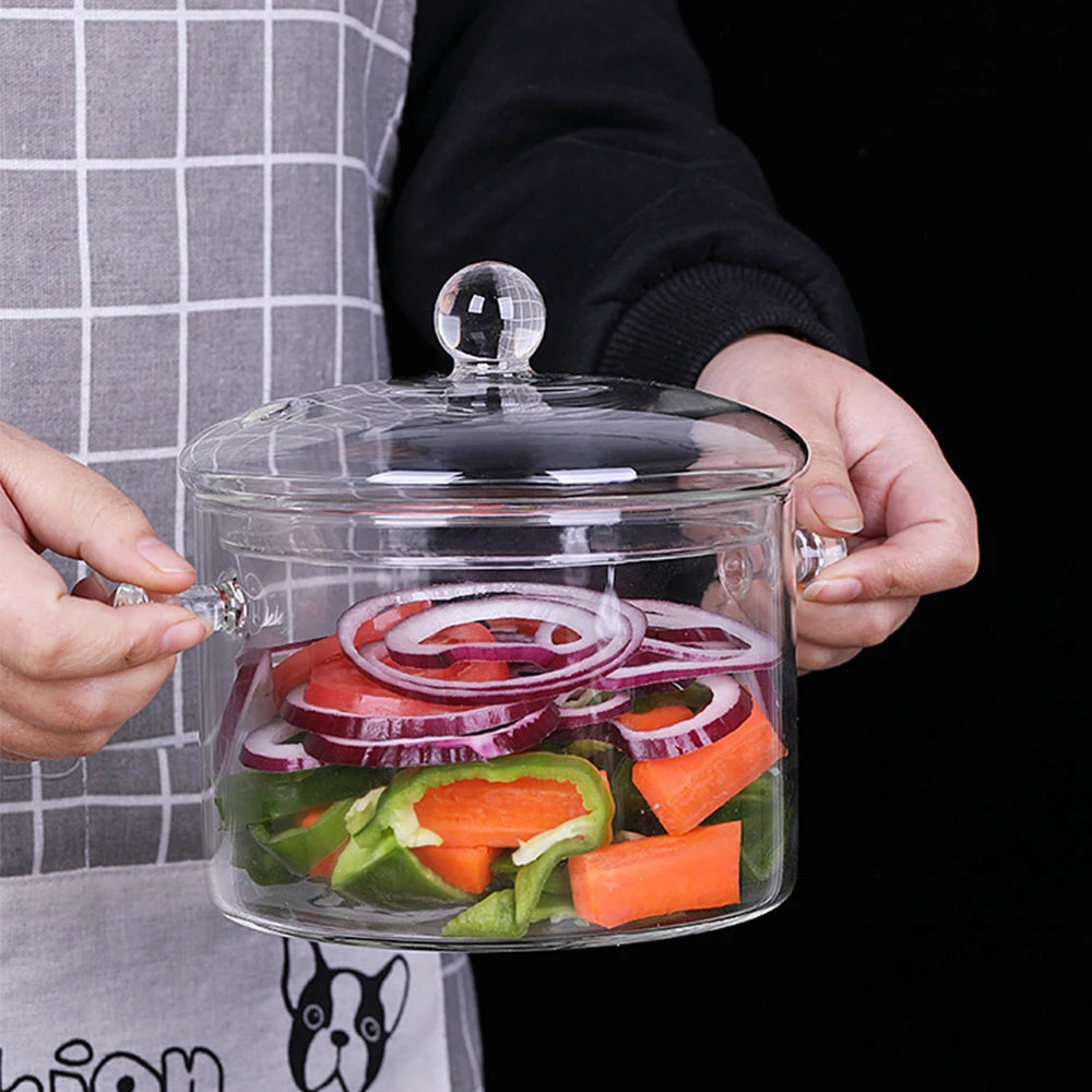 Una mano sostiene una olla de vidrio transparente llena de verduras cortadas para cocinar.