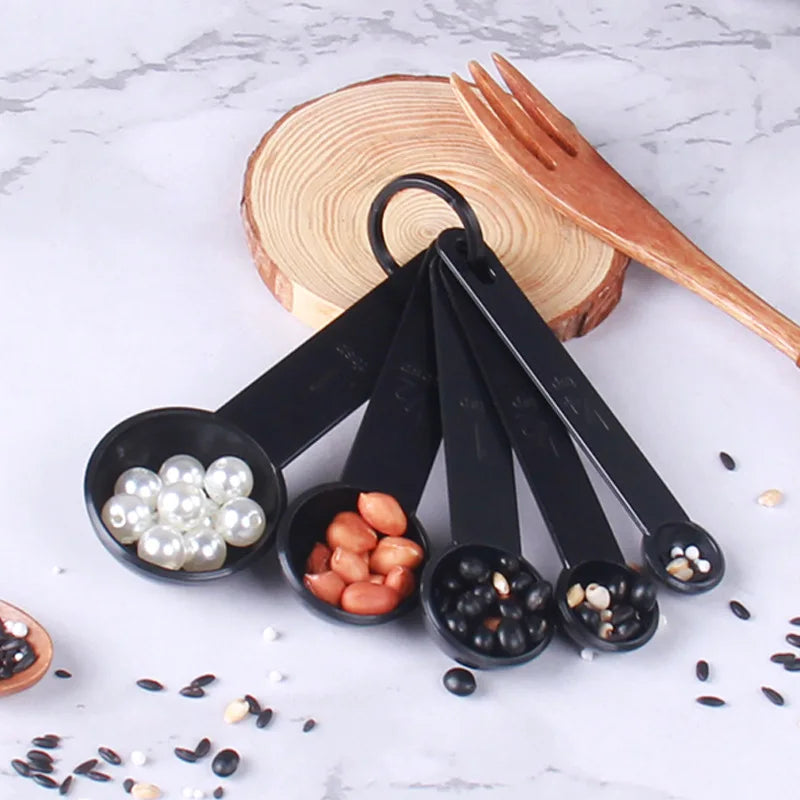 A set of black precision kitchen measuring spoons and a wooden cutting board with various seeds and nuts.