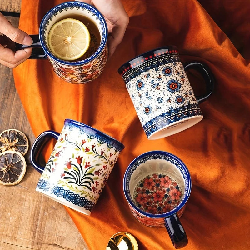 A close-up of several bohemian floral ceramic mugs filled with tea or liquid, resting on an orange fabric.