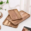 A set of natural acacia wood serving trays stacked and displayed on a white surface.