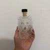 Un decantador de whisky cristalino con forma de cabeza de lobo y un tapón negro, sostenido en una mano.