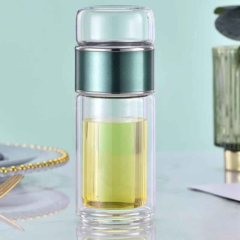 A double-layer borosilicate glass tea infuser with a clear glass body and a teal colored cap, filled with yellow-green liquid