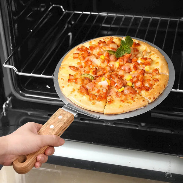 Eine Hand benutzt einen runden Edelstahl-Pizza-Schieber mit Holzgriff, um eine frisch gebackene Pizza aus einem Ofenrost zu h