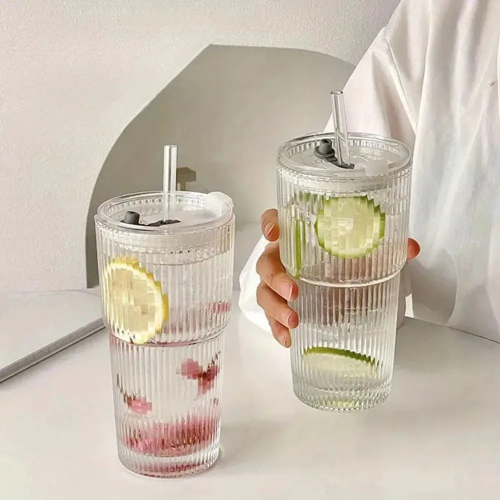 A clear glass drinking cup filled with pink liquid and lime slices, held by a hand.
