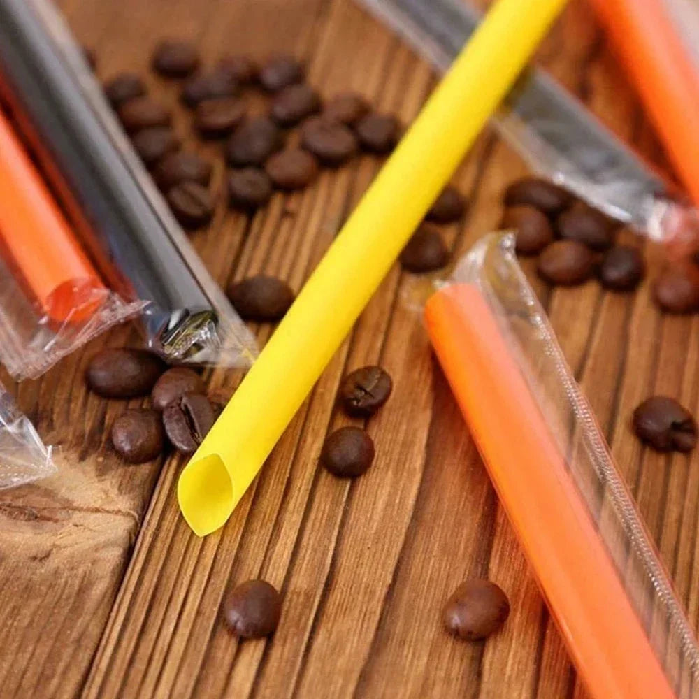 A collection of reusable plastic drinking straws in various colors, including yellow and orange, scattered on a wooden surfac