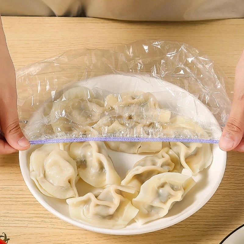 A hand is holding a clear plastic food cover over a white plate filled with steamed dumplings.