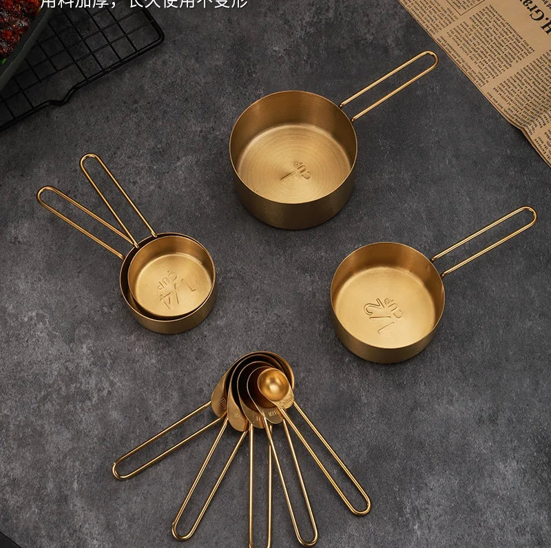 A set of brass or gold-toned stainless steel measuring cups and spoons arranged on a dark gray surface.