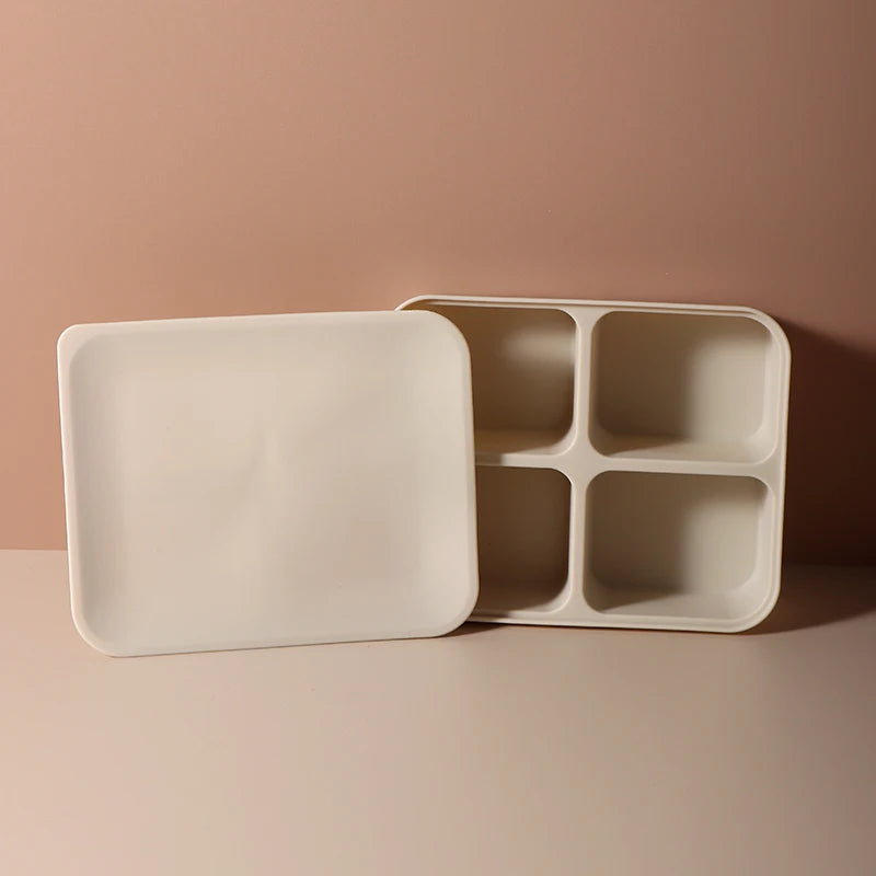 A white silicone food tray divided into four sections is shown on a light pink surface.