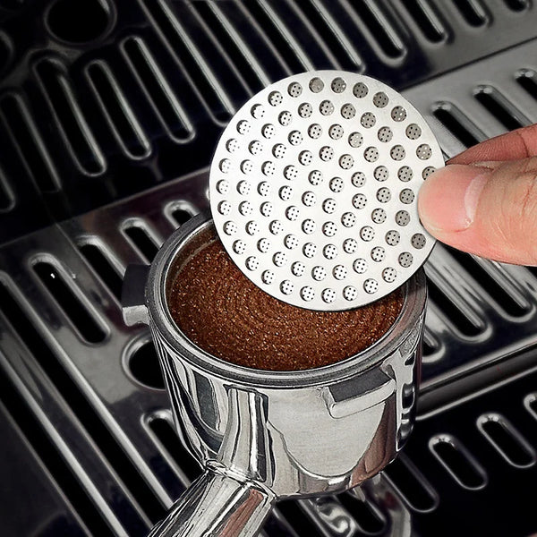Eine Hand legt eine wiederverwendbare Metall-Espresso-Puck-Sieb auf eine silberne Kaffeetasse.