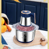 A stainless steel electric meat grinder is shown with minced meat and fresh ingredients on a cutting board.