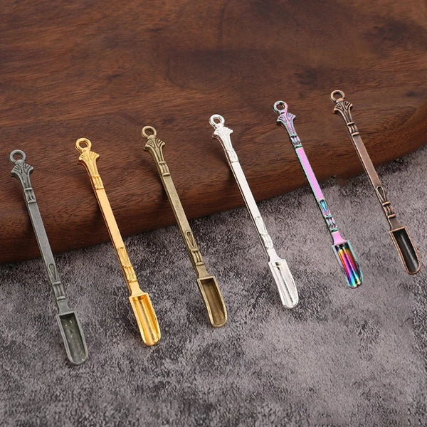 Eine Sammlung von Metall-Mini-Schaufeln und Löffeln in verschiedenen Farben, präsentiert auf einer dunklen Holzoberfläche.