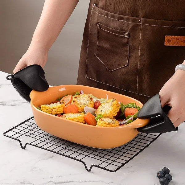 Eine Hand benutzt einen schwarzen Silikon-Ovenhandschuh, um Essen aus einer orangen Keramikschale auf einem Drahtrost zu hebe