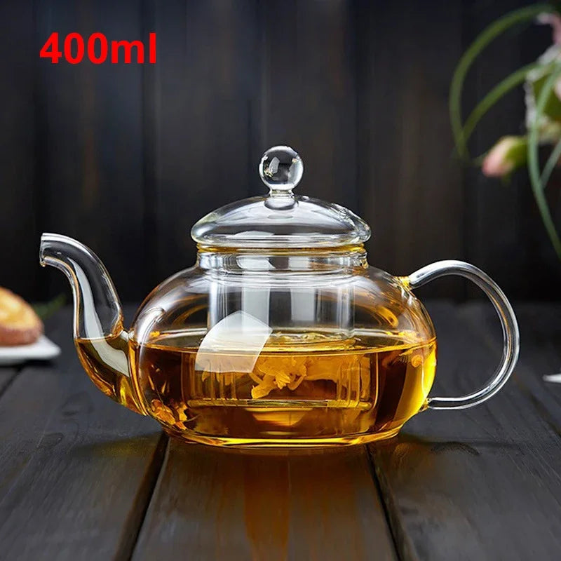 A clear glass teapot with a lid and handle filled with amber tea on a dark wooden surface.