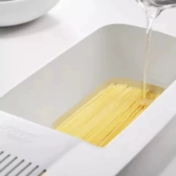 Wiederverwendbarer Plastik-Nudelsüblicher und Kocher mit Wasser, das in einen weißen Behälter mit trockenem Spaghetti tropft