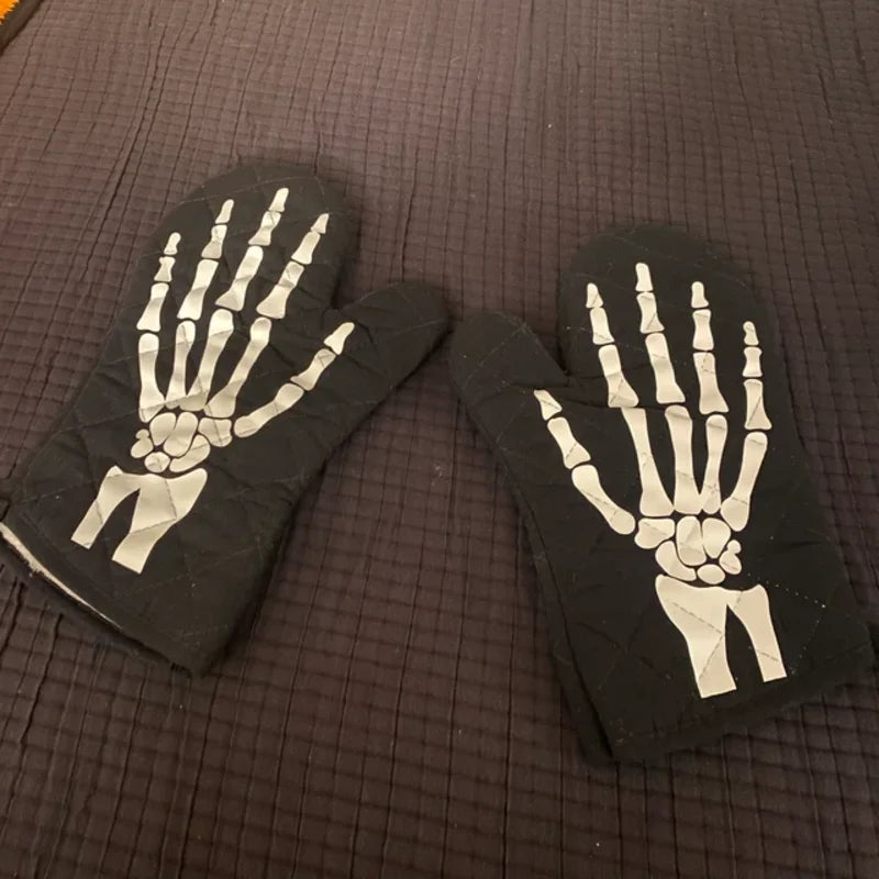 A pair of black oven mitts featuring white skeleton hand designs for Halloween kitchen decor.