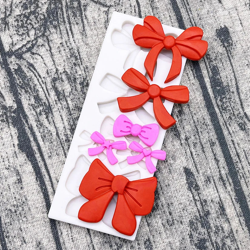 A white silicone baking mold tray with various colored paper or silicone bows for decorating cupcakes.