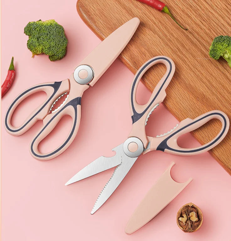 Un juego de tijeras y un cuchillo de acero inoxidable rosa y plateado sobre una tabla de cortar con verduras.