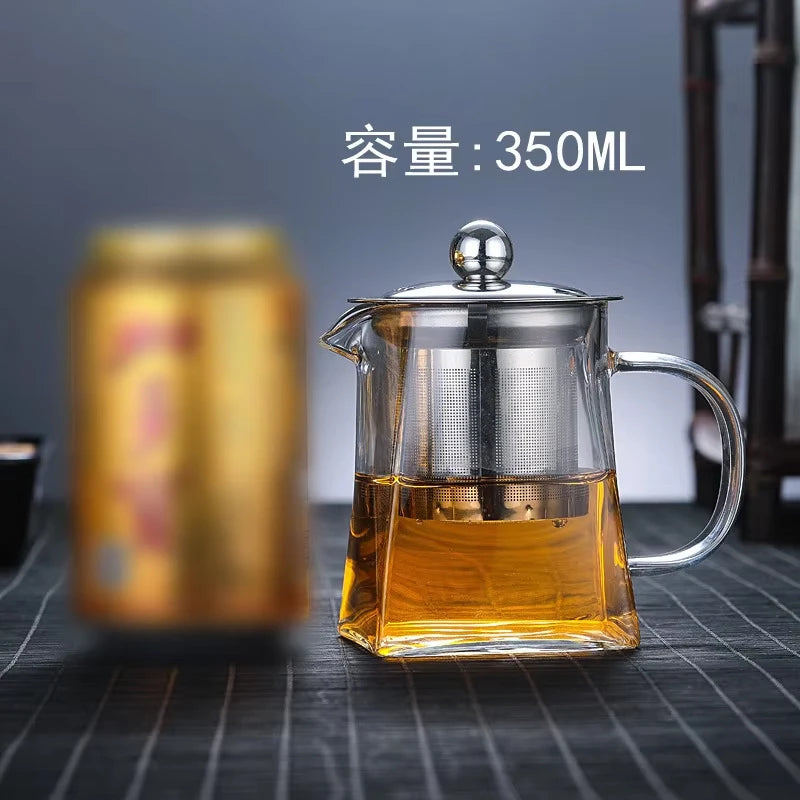 A clear glass teapot with a stainless steel infuser is filled with amber tea, set against a dark background.