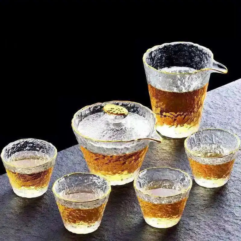 A set of elegant glass tea cups and a teapot are displayed on a dark surface.