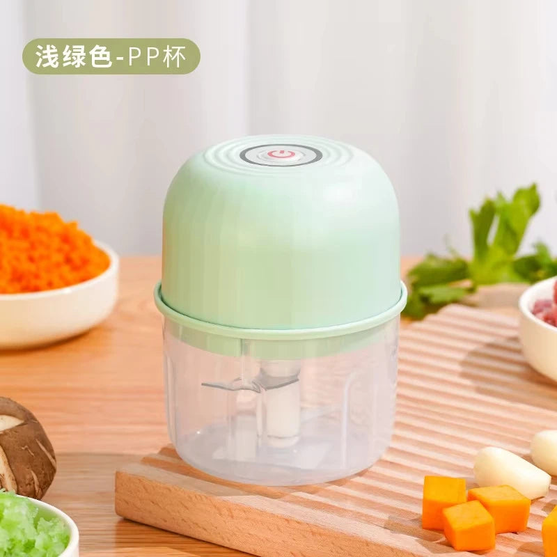 A clear plastic electric grinder with a light green lid and base, resting on a wooden cutting board.