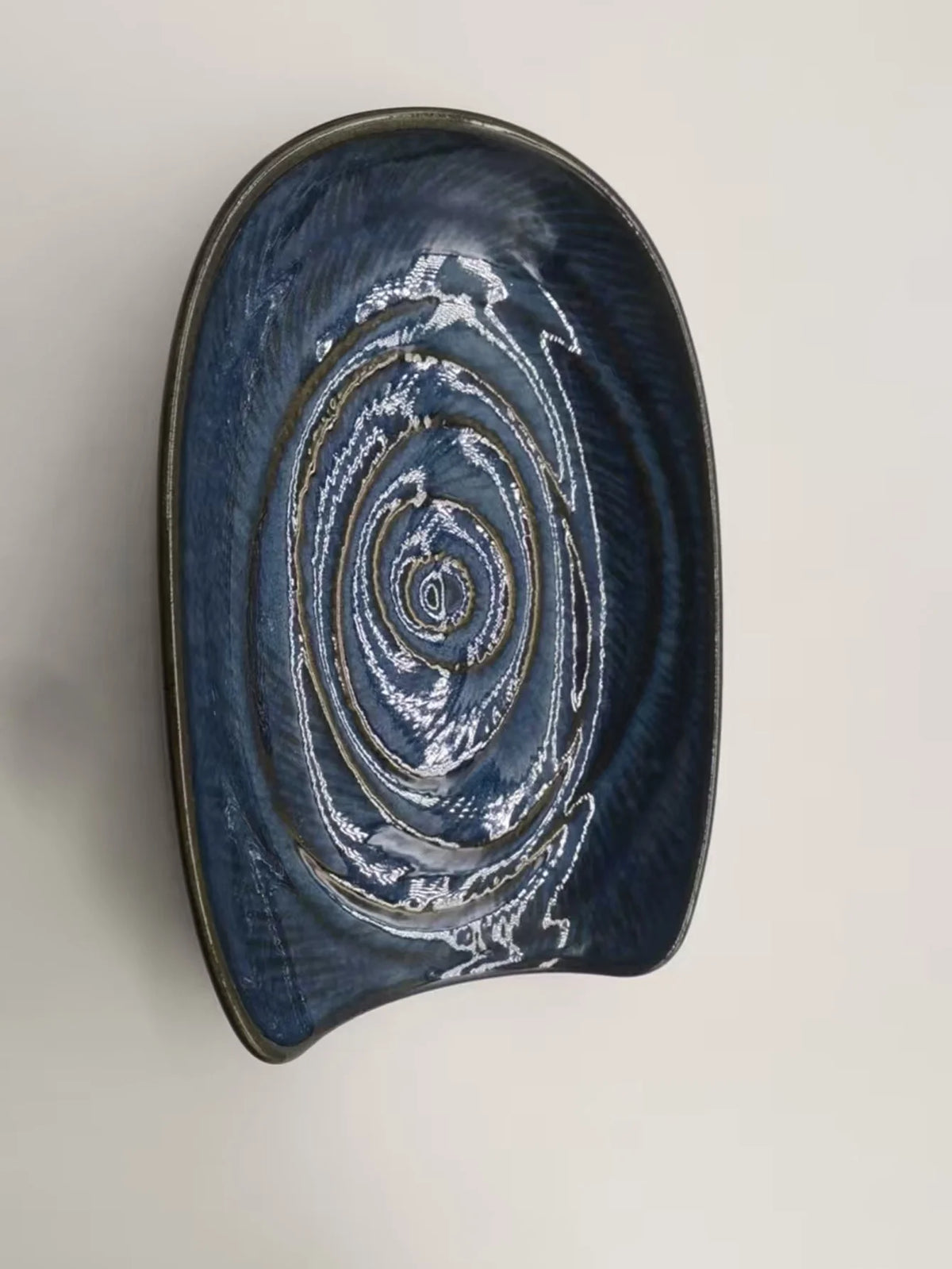 A dark blue ceramic cutlery holder with concentric swirling patterns and a gold rim.