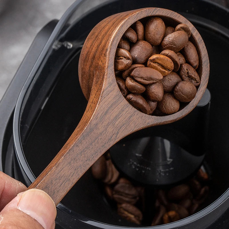 A wooden coffee measuring spoon filled with roasted coffee beans is shown inside a black container.