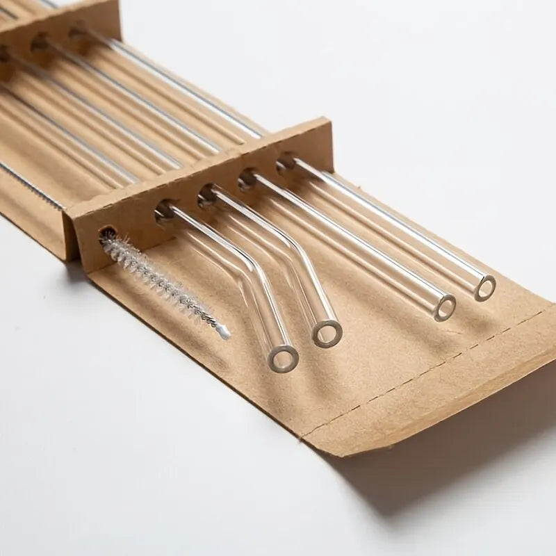 A set of five clear glass straws are arranged in a cardboard holder.