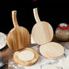 A solid wood dumpling press tool is shown with its lid open, revealing a round wooden base and a white dough disc.