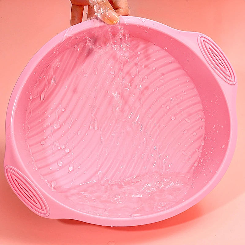 A pink nonstick silicone baking pan is being filled with water by a hand.