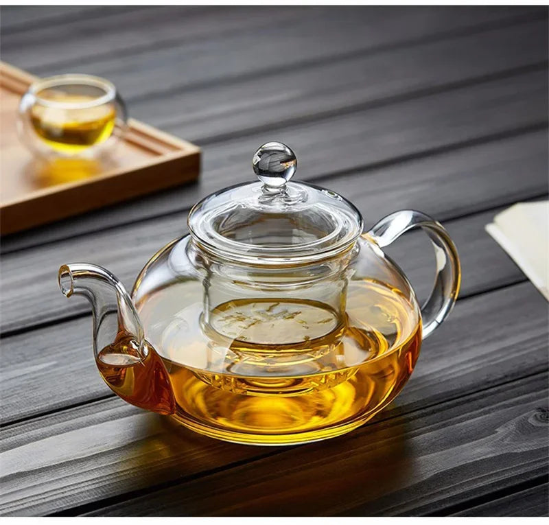 A clear glass teapot filled with amber tea is sitting on a dark wooden surface.