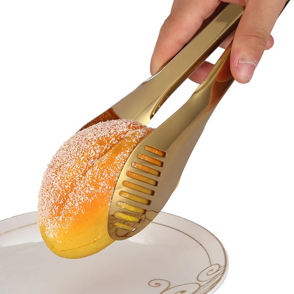 Eine Hand hält goldfarbene Edelstahl-Grillzangen und -Klemmen über einem weißen Teller.