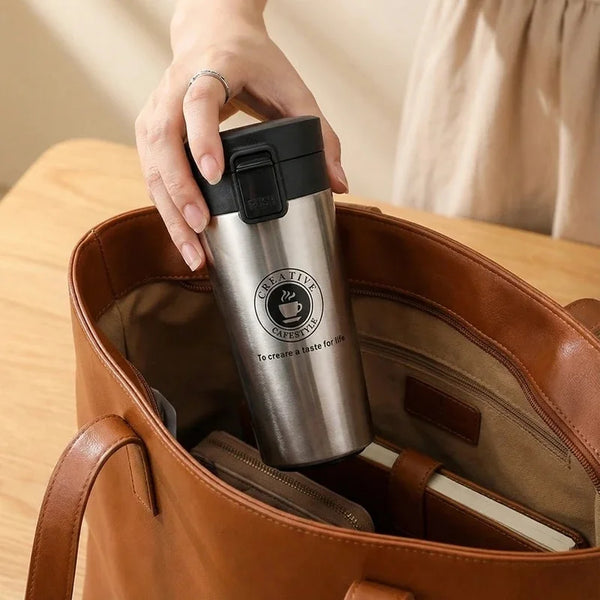 Eine Hand hält eine Edelstahl-Thermokanne in einer braunen Leder-Tasche.