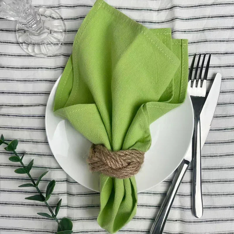 A stack of bright lime green reusable cotton cloth napkins tied with natural twine on a white plate set against a striped clo