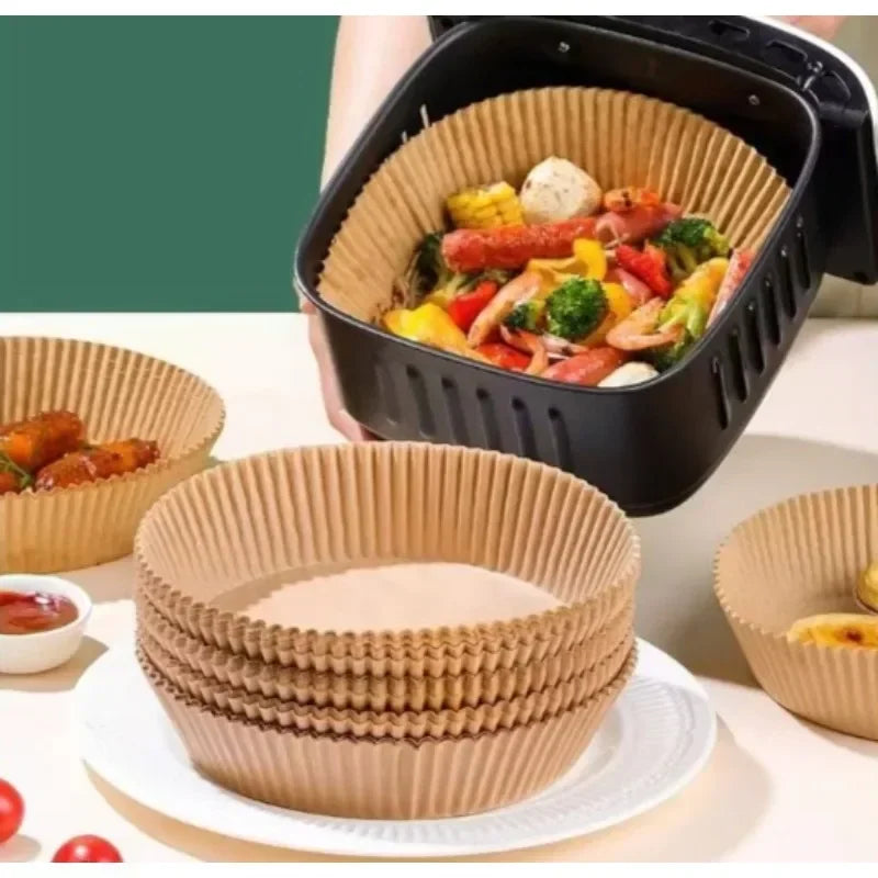 A black disposable non-stick cooking liner is shown filled with colorful roasted vegetables, next to stacked paper liners.