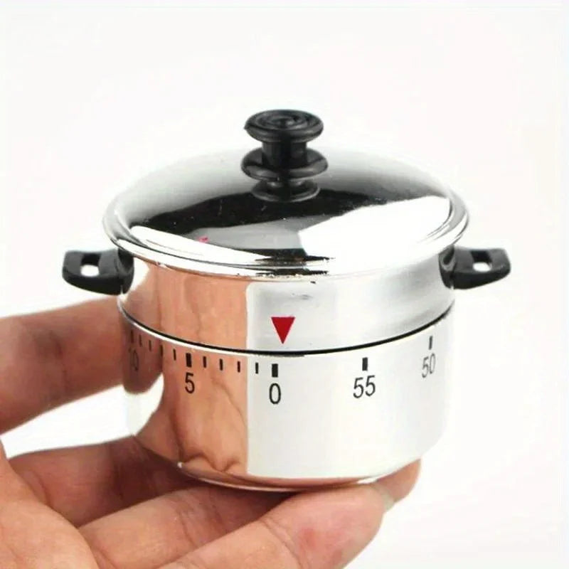 A hand holds a stainless steel mechanical kitchen cooking timer with a red indicator and numbered markings.