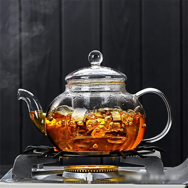 A clear glass tea pot is heating on a stovetop, releasing steam and amber liquid.