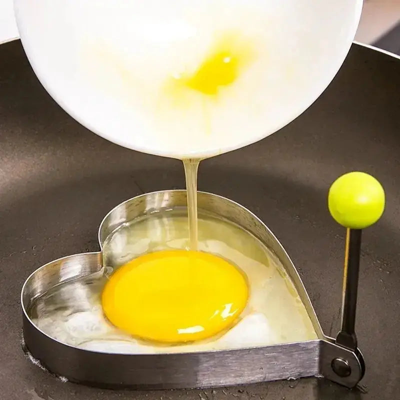 A stainless steel mold is dripping a liquid from a fried egg into a pan.
