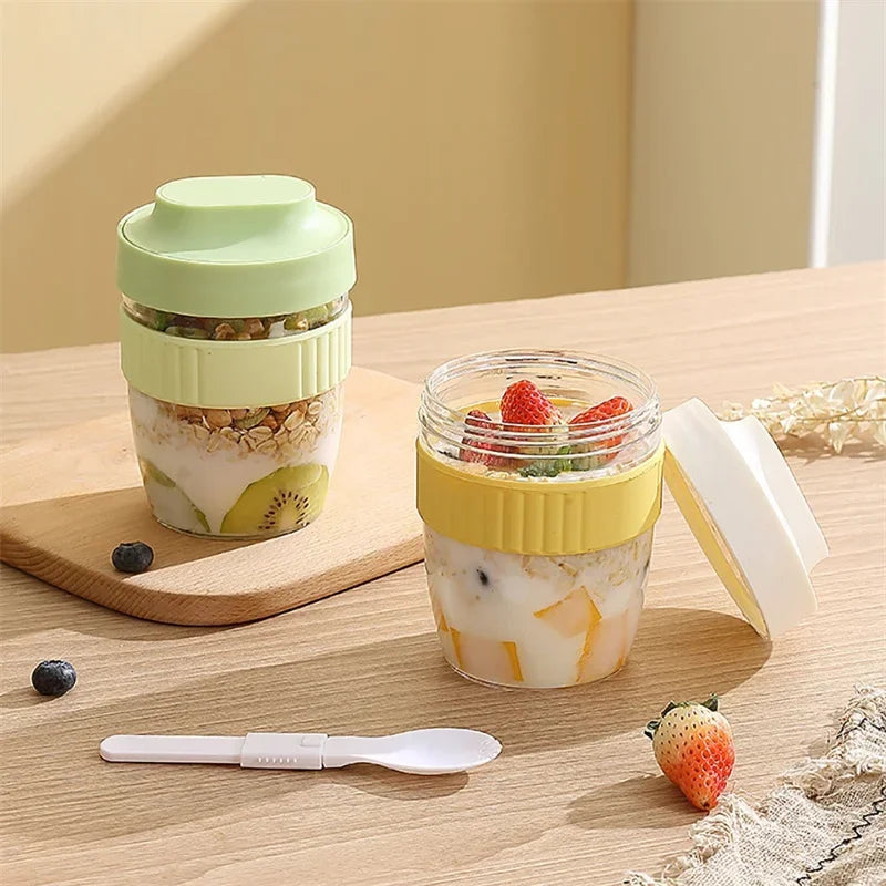 A glass jar of iced beverage in a green container sits next to a yellow lid and a strawberry on a wooden surface.