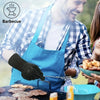 A man wearing a blue apron is using black heavy-duty BBQ mitts to cook food on a grill.