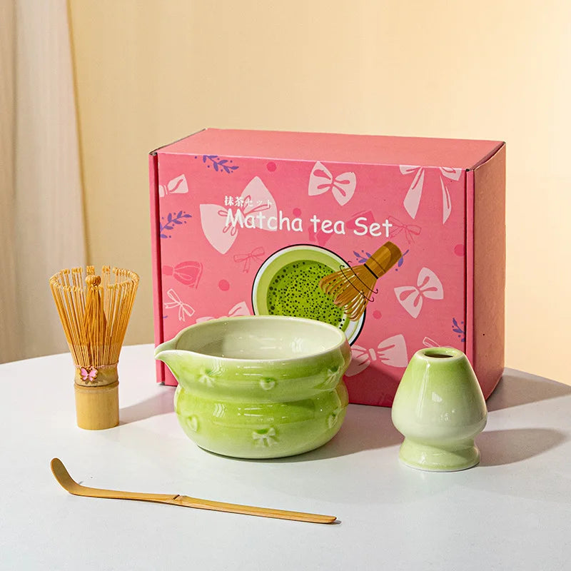 A pink box containing a matcha tea set with a ceramic bowl and bamboo whisk on a white surface.