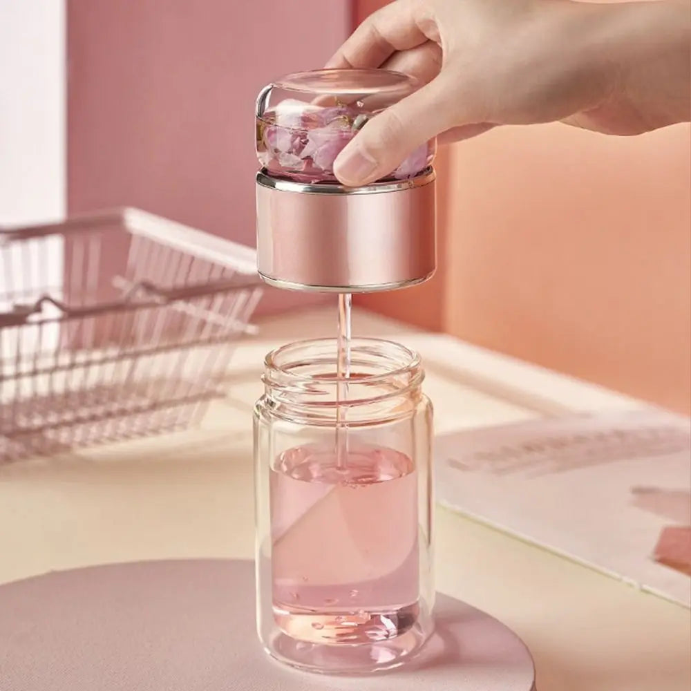 A hand is using a metal tea infuser to pour pink liquid into a glass jar for tea infusion.