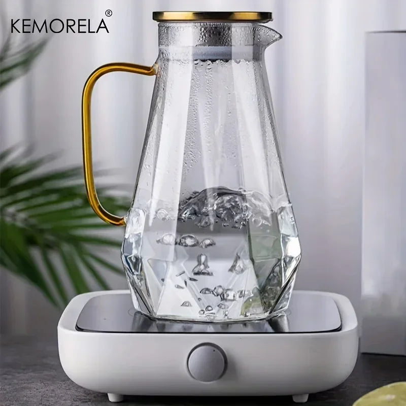 A clear glass pitcher with a gold handle sits on a white electric water dispenser base.