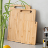 A light wood bamboo kitchen cutting board is shown next to a green plant.
