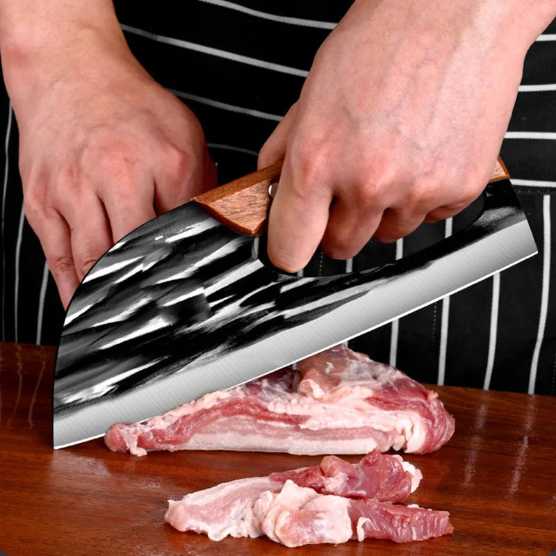 Hands holding a hand-forged stainless steel chef knife with a wooden handle slicing raw meat on a wooden board.